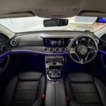 Luxurious interior of Mercedes E-Class featuring purple ambient lighting and widescreen cockpit.