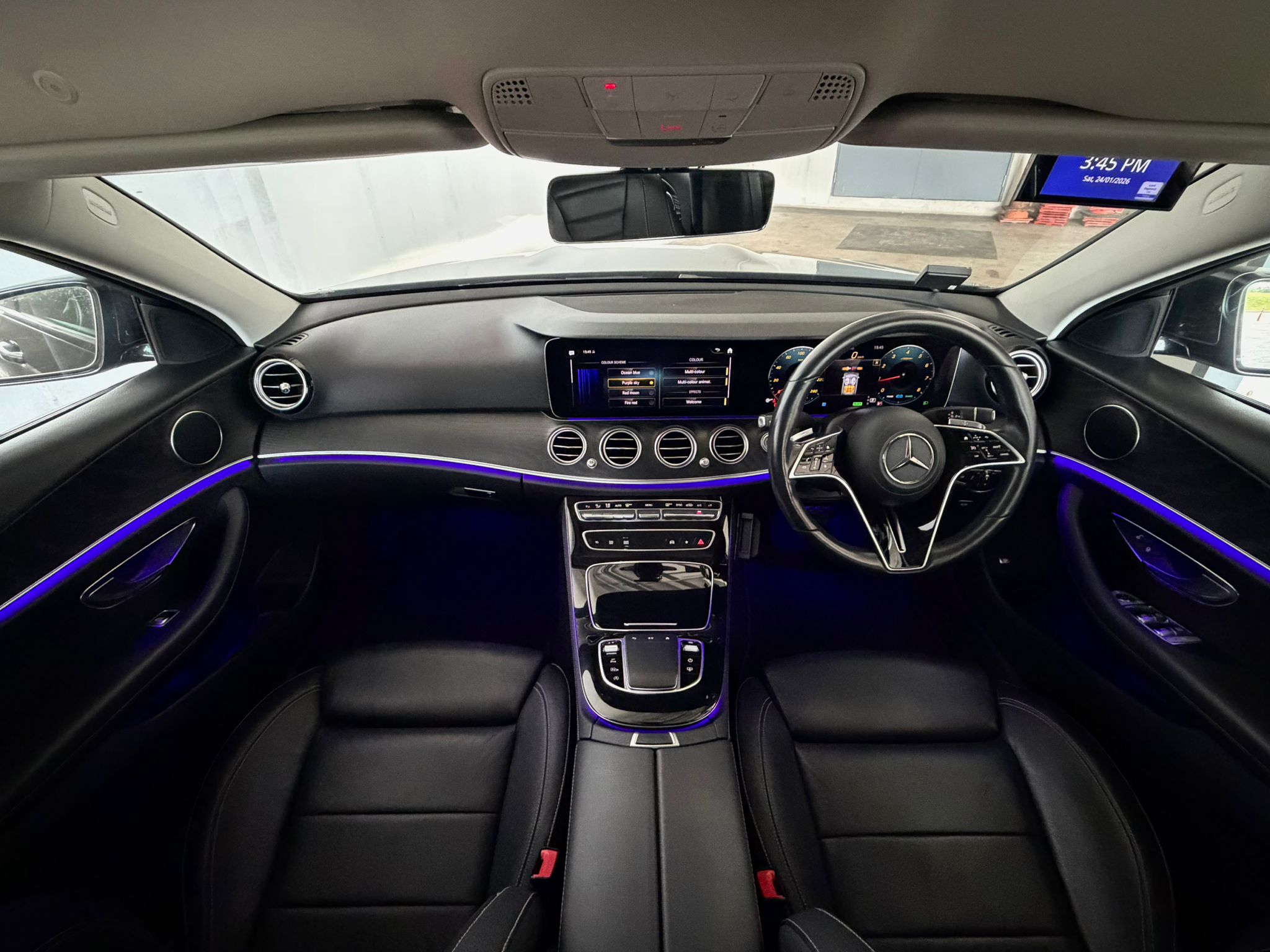Luxurious interior of Mercedes E-Class featuring purple ambient lighting and widescreen cockpit.