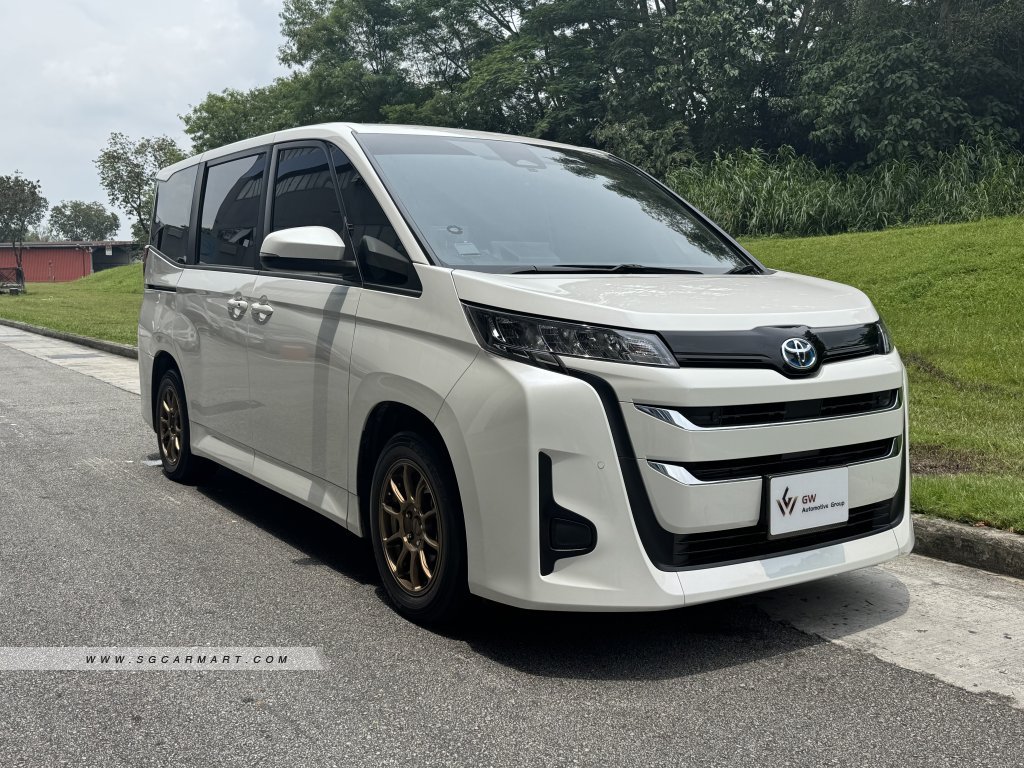 Front three-quarter view of a white 2024 Toyota Noah Hybrid 1.8A X with bronze sports rims.