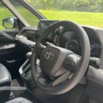 Interior cockpit view of the Toyota Noah Hybrid showing the multifunctional steering wheel and touchscreen head unit.