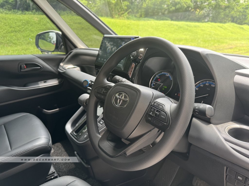 Interior cockpit view of the Toyota Noah Hybrid showing the multifunctional steering wheel and touchscreen head unit.
