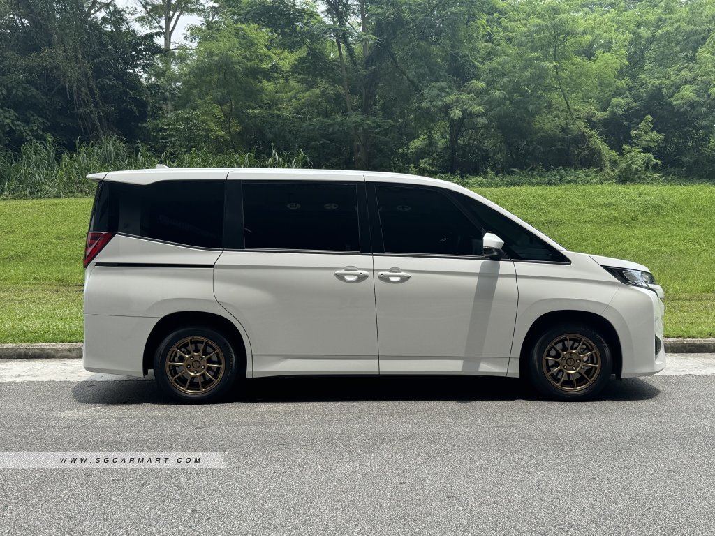 Side profile of a Toyota Noah Hybrid featuring a high-roof design and dual power sliding doors.